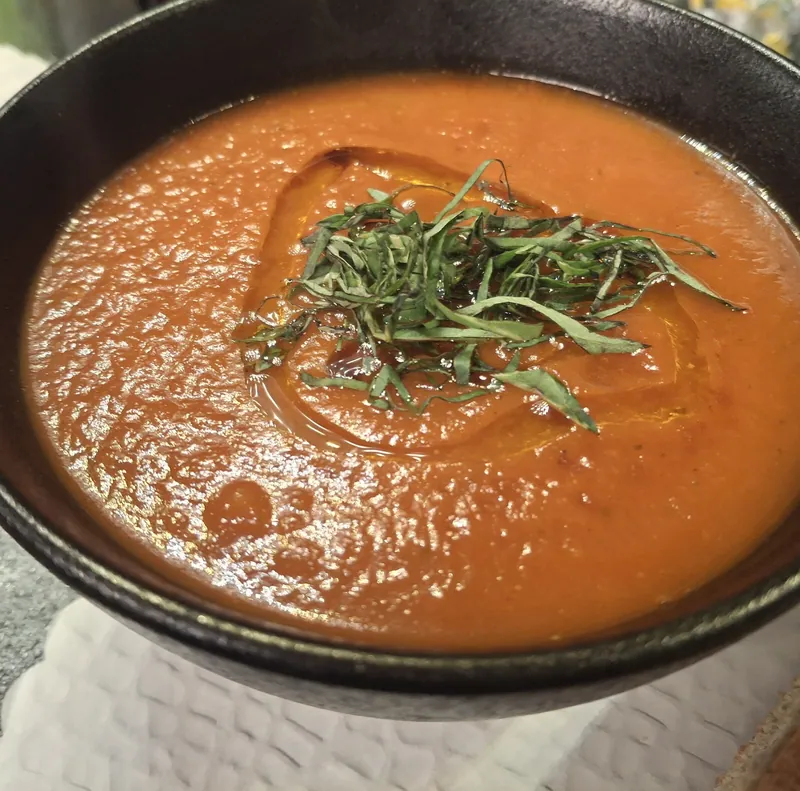 Tomatensuppe im dunklen Teller mit frischen Kräutern